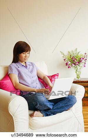 Stock Photo - Young woman sitting in an armchair and working on a laptop. Fotosearch