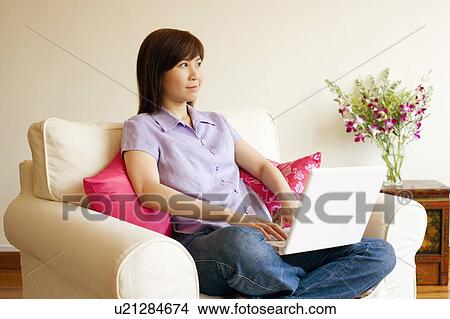 Picture - Young woman sitting in an armchair with a laptop. Fotosearch