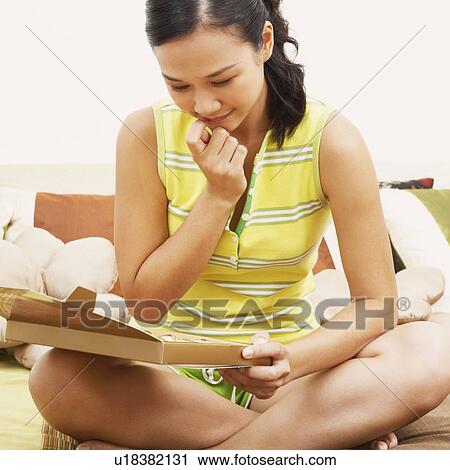 Stock Image - Young woman sitting on the bed and looking at a box of chocolates. Fotosearch