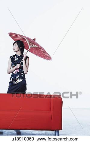 Stock Photo - Young woman standing behind a couch holding a parasol. Fotosearch