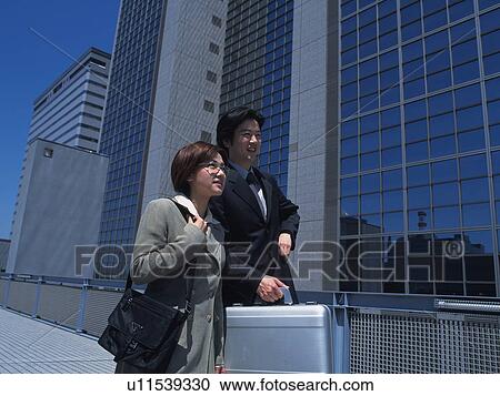 Businessman and businesswoman looking at something by the high rise building, Low Angle View View Large Photo Image Stock Image - Businessman and businesswoman looking at something by the high rise building, Low Angle View. Fotosearch