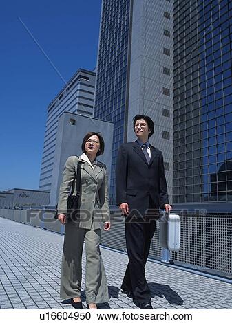 Stock Image - Businessman and businesswoman looking away by the high rise building, Low Angle View. Fotosearch
