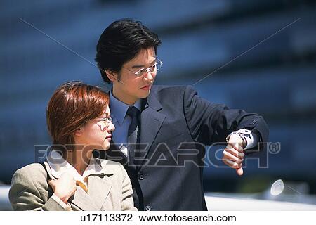 Stock Image - Businessman and businesswoman looking at watch, Pin Focus. Fotosearch
