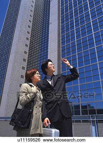 Stock Photograph - Businessman and businesswoman pointing and looking at something by the high rise building, Low Angle View. Fotosearch