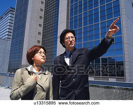 Stock Photography - Businessman and businesswoman pointing and looking at something by the high rise building, Low Angle View. Fotosearch