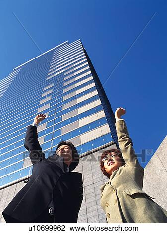 Stock Image - Businessman and businesswoman raising fist up in the air near the high rise building, Low Angle View. Fotosearch