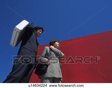 Picture - Businessman and businesswoman standing by the red Wall, Low Angle View. Fotosearch