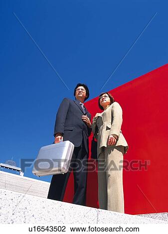 Businessman and businesswoman standing by the red Wall, Low Angle View View Large Photo Image Stock Image - Businessman and businesswoman standing by the red Wall, Low Angle View. Fotosearch