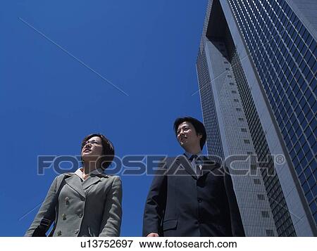 Businessman and businesswoman standing by the high rise building and looking away, Low Angle View View Large Photo Image Stock Photo - Businessman and businesswoman standing by the high rise building and looking away, Low Angle View. Fotosearch