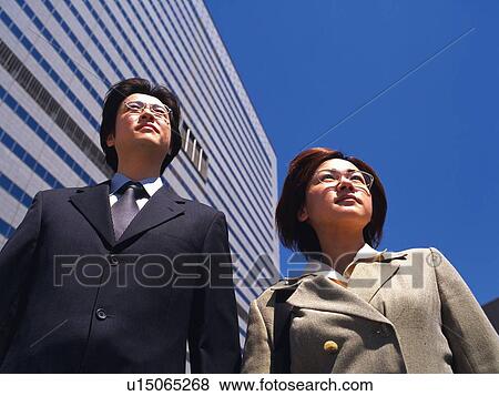 Businessman and businesswoman standing by the high rise building and looking away, Low Angle View View Large Photo Image Stock Photo - Businessman and businesswoman standing by the high rise building and looking away, Low Angle View. Fotosearch