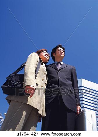 Businessman and businesswoman standing and looking away near the high rise building, Low Angle View View Large Photo Image Stock Photo - Businessman and businesswoman standing and looking away near the high rise building, Low Angle View. Fotosearch