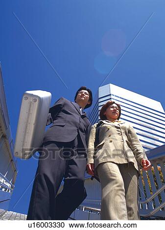 Stock Image - Businessman and businesswoman walking down the stairs, Low Angle View. Fotosearch
