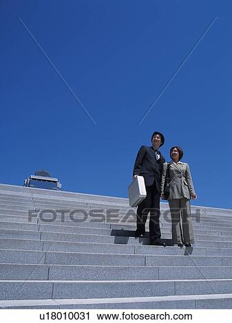 Stock Image - Businessman and businesswoman walking down the stairs, Low Angle View. Fotosearch