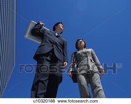 Stock Photo - Businessman and businesswoman walking by the high rise building, Low Angle View. Fotosearch