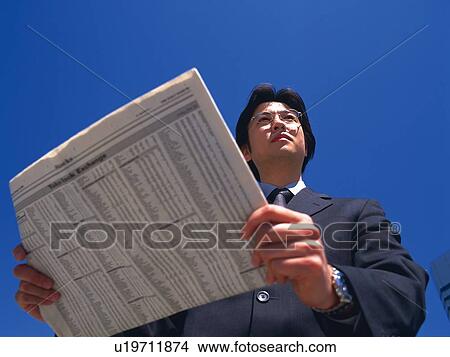 Picture - Businessman looking away and holding news paper, Low Angle View. Fotosearch
