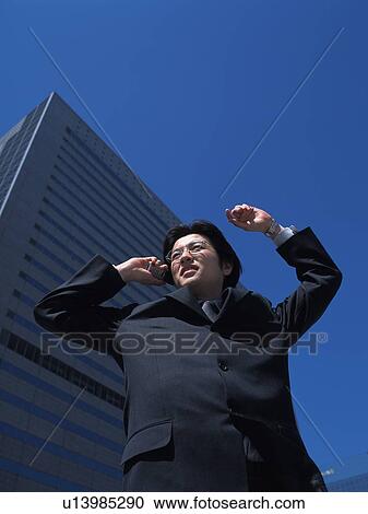 Stock Image - Businessman looking away and holding mobile phone, Low Angle View. Fotosearch