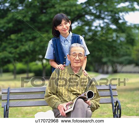 Stock Photo - Grandfather sitting on a bench and granddaughter standing behind, Front View. Fotosearch
