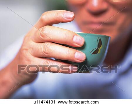 Stock Image - Hand of the senior adult man holding a cup of tea, Close Up. Fotosearch