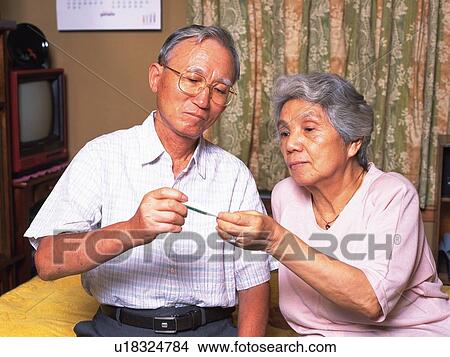 Picture - Senior adult man and woman reading thermometer, Front View. Fotosearch
