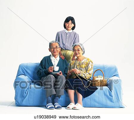Stock Photo - Senior adult man and woman sitting together on a sofa and a granddaughter standing behind, Front View. Fotosearch