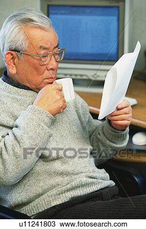 Stock Image - Senior adult man reading documents with a cup in hand, Side View. Fotosearch