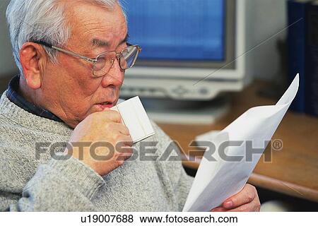 Stock Photo - Senior adult man reading documents with a cup in hand, Side View. Fotosearch