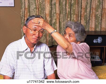 Stock Image - Senior adult woman checking husband's temperature, Front View. Fotosearch