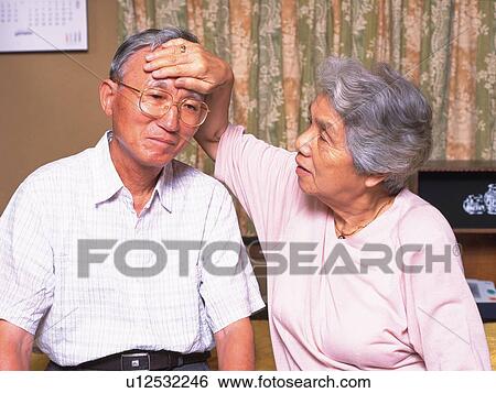 Stock Photograph - Senior adult woman checking husband's temperature, Front View. Fotosearch