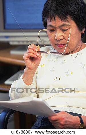 Stock Photo - Senior adult woman reading documents, Front View. Fotosearch