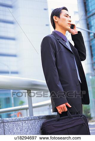 Stock Photo - bag, mobile phone, young adult, asian ethnicity, man only, building exterior. Fotosearch