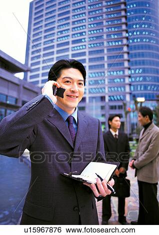 Stock Photograph - well dressed, business in asia, on the phone, asian ethnicity. Fotosearch