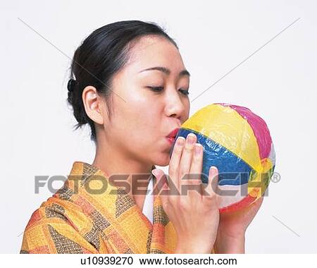 Stock Image - A woman in kimono blowing up a Japanese paper balloon, Side View. Fotosearch