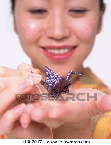 Stock Image - A woman in kimono holding an origami crane in hands, Close Up, Front View, Differential Focus. Fotosearch