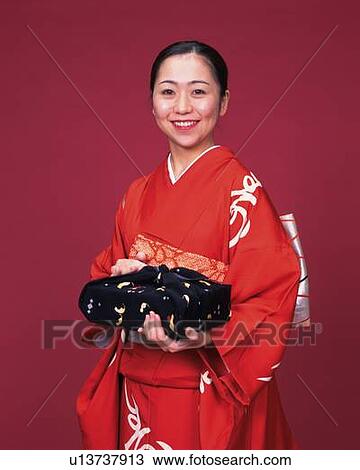 Stock Image - A woman in kimono smiling and holding a gift, Front View. Fotosearch