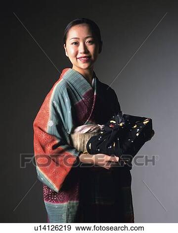 Stock Photo - A woman in kimono smiling and holding a gift, Front View. Fotosearch