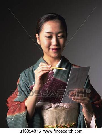 Stock Photography - A woman in kimono writing on firm paper, Front View. Fotosearch