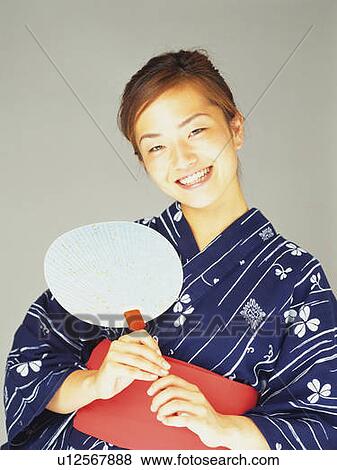 Stock Photo - A woman in yukata smiling and holding a fan, Front View. Fotosearch