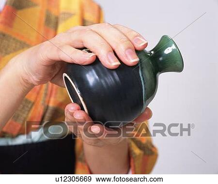 Stock Photo - Hands of a woman in kimono serving sake, Close Up. Fotosearch