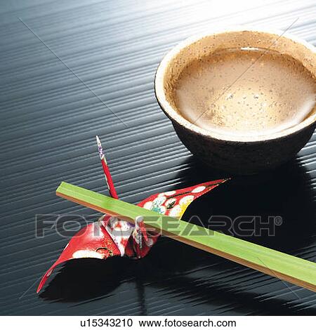 Stock Image - Cold sake in cup and bamboo chopsticks on Origami bird, high angle view. Fotosearch