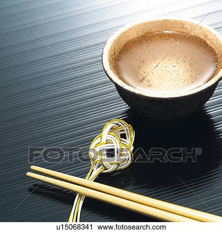 Stock Image - Cold sake in cup and chopsticks on holder, high angle view. Fotosearch