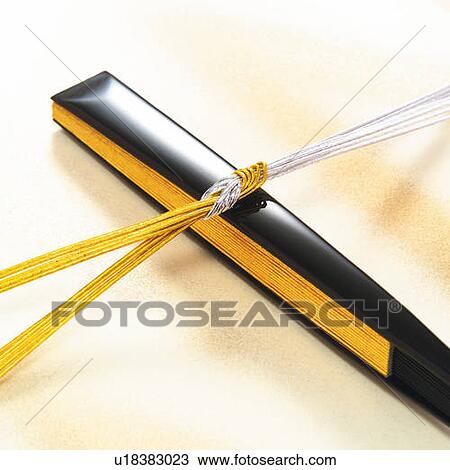 Stock Image - Gold and silver strings put on folded Japanese fan, high angle view. Fotosearch