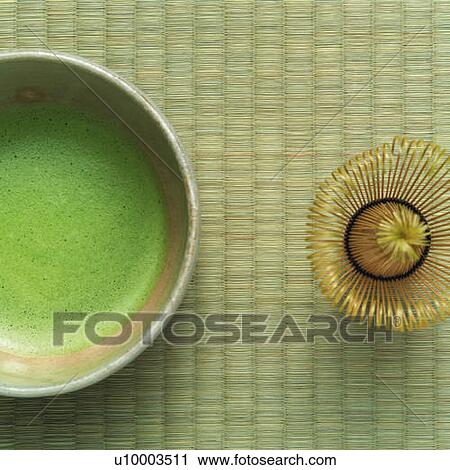 Stock Image - Japanese tea in bowl and tea whisk on Tatami mat, high angle view, Japan. Fotosearch
