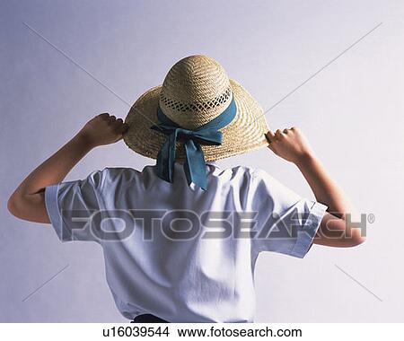 Picture - Boy wearing straw hat holding the edge of the hat, rear view, white background. Fotosearch