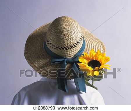 Stock Image - Boy wearing straw hat with sunflower, rear view, white background. Fotosearch