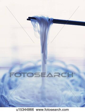 Stock Photograph - Chopsticks holding noodles out of glass bowl, high angle view, differential focus. Fotosearch