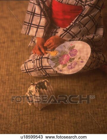 Stock Image - Pig-shaped incense burner and woman in yukata sitting and holding a Japanese fan, high angle view, composition. Fotosearch
