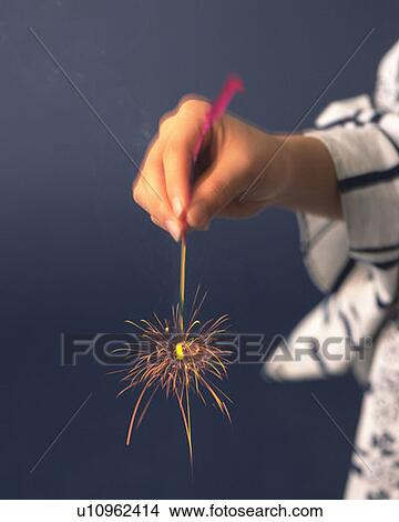 Picture - Woman in yukata holding a lighting firework, side view, blue background, differential focus, blurred motion. Fotosearch
