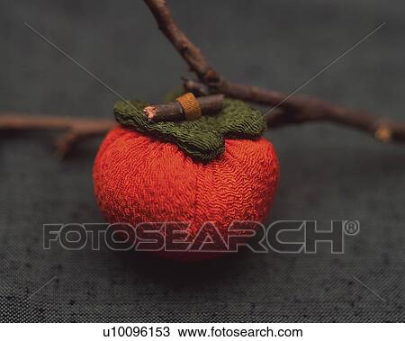 Stock Image - Branch and toy persimmon on fabric, high angle view, differential focus. Fotosearch