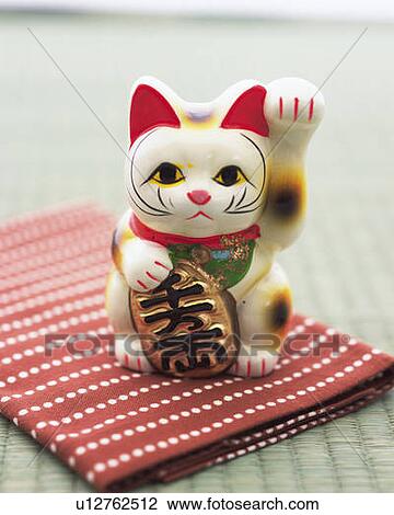 Stock Image - Doll of cat with a beckoning paw on fabric, high angle view, differential focus. Fotosearch