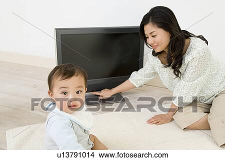 Picture - Baby and Mother Sitting on Floor, Mother Turning Off the TV. Fotosearch